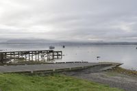 two people walking down an old concrete walkway near the water and bridge on a cloudy day