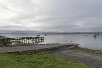 two people walking down an old concrete walkway near the water and bridge on a cloudy day