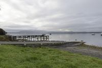 two people walking down an old concrete walkway near the water and bridge on a cloudy day