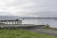 two people walking down an old concrete walkway near the water and bridge on a cloudy day