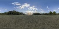 the wide open field with a large cloud in the sky at dusk near a lake