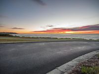 a view of the ocean and a beautiful sunset from behind a car on a roadway