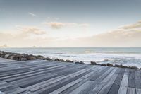 a dock with a person on the beach in the distance and the ocean water in the background