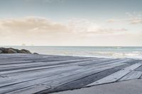 a dock with a person on the beach in the distance and the ocean water in the background