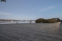 wooden boardwalk next to water with boats in the distance on a cloudy day in autumn