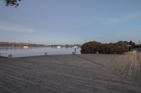 wooden boardwalk next to water with boats in the distance on a cloudy day in autumn