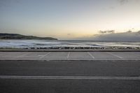 an empty parking lot next to a beach with waves coming in the distance at sunset