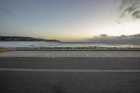 an empty parking lot next to a beach with waves coming in the distance at sunset