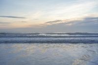 an evening sky with clouds and ocean waves crashing up to a beach area, with a person standing in the water