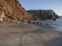 a stone walkway leading to a rocky coastline near the water's edge with a beach in the foreground