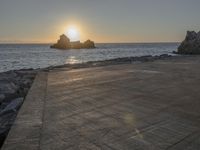 a skateboarder is doing tricks next to a rocky shore at dusk on a sunny day