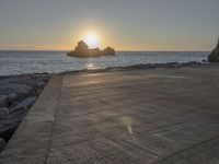 a skateboarder is doing tricks next to a rocky shore at dusk on a sunny day