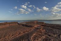 the beach is covered in rocks and boulders, with clouds above them and water running along it