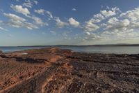 the beach is covered in rocks and boulders, with clouds above them and water running along it