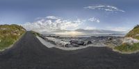 a panorama of a beach with rocks, water, and a rock road at the shore