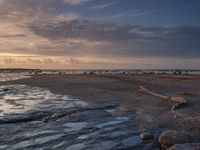 an old photo of a beach with some rocks and water in the sand at sunset