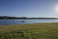 a small boat is in the water with grass on the shore in front of a lake