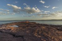 a photo of the sun over a rocky shore with a boat on it at the horizon