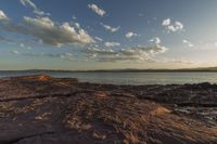 a photo of the sun over a rocky shore with a boat on it at the horizon