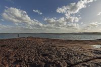 a couple is walking by the ocean along a rocky shore while onlookers watch