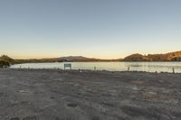 a field is in front of some water with a bench in the center and mountains