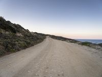 gravel road in front of water with cliffs below at dusk in remote area of arid land