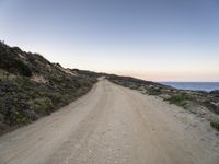 gravel road in front of water with cliffs below at dusk in remote area of arid land