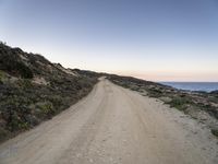 gravel road in front of water with cliffs below at dusk in remote area of arid land