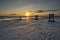 the sun is setting on a beach with two blue sign posts in the sand and two signs left by the ocean