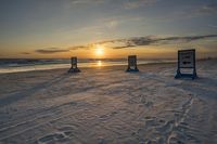 the sun is setting on a beach with two blue sign posts in the sand and two signs left by the ocean