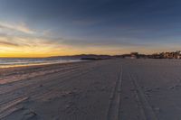 the sun setting on a beach by the ocean at sunset with tracks left by the people on the sand