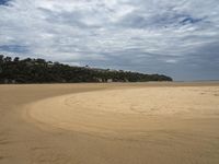 an empty sandy beach next to the ocean with trees in the distance and a hill in the distance