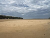 an empty sandy beach next to the ocean with trees in the distance and a hill in the distance