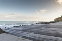 wooden walkway by the water with waves crashing in to the shore of the ocean,