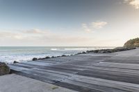 wooden walkway by the water with waves crashing in to the shore of the ocean,