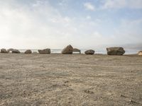 six large rocks that are sitting in the sand at the beach, one of them upside down, are standing in the middle