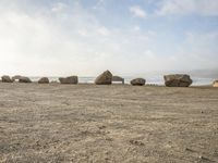 six large rocks that are sitting in the sand at the beach, one of them upside down, are standing in the middle