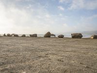 six large rocks that are sitting in the sand at the beach, one of them upside down, are standing in the middle