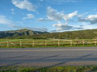 a lone country road is in the countryside area with mountains on both sides and barbed fence between the two sides