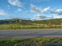 a lone country road is in the countryside area with mountains on both sides and barbed fence between the two sides