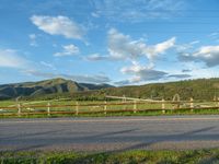 a lone country road is in the countryside area with mountains on both sides and barbed fence between the two sides