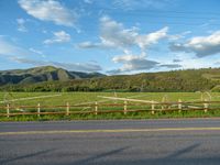 a lone country road is in the countryside area with mountains on both sides and barbed fence between the two sides