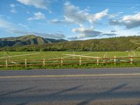 a lone country road is in the countryside area with mountains on both sides and barbed fence between the two sides