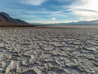 the desert is dry with no one in it and the mountains in the distance are covered by cloud