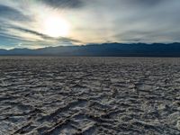 a photograph of the sun over a salt field with mountains behind it and waves and clouds