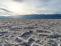 a photograph of the sun over a salt field with mountains behind it and waves and clouds