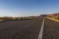 a long stretch of road is winding through a desert area in front of a mountain and cliffs