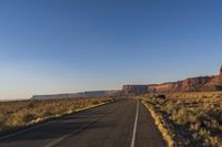 a long stretch of road is winding through a desert area in front of a mountain and cliffs