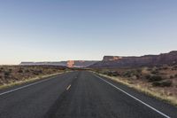 a long open road winding through the desert on a beautiful day with sparse shrubs and trees