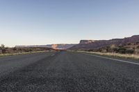 a long open road winding through the desert on a beautiful day with sparse shrubs and trees